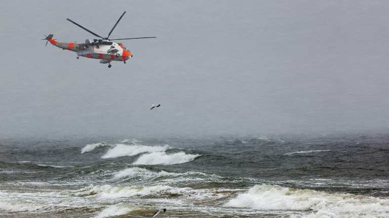 A helicopter flying over choppy seas as a rescue serviceman hangs below.